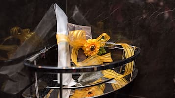 A glass display case with a folded white napkin, a yellow flower, and a yellow ribbon.