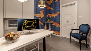 Een moderne kamer met een grote flatscreen-tv op een witte tafel, een decoratieve schaal met bloemen, een blauwe stoel en een muur met een muurschildering van een gouden arend.