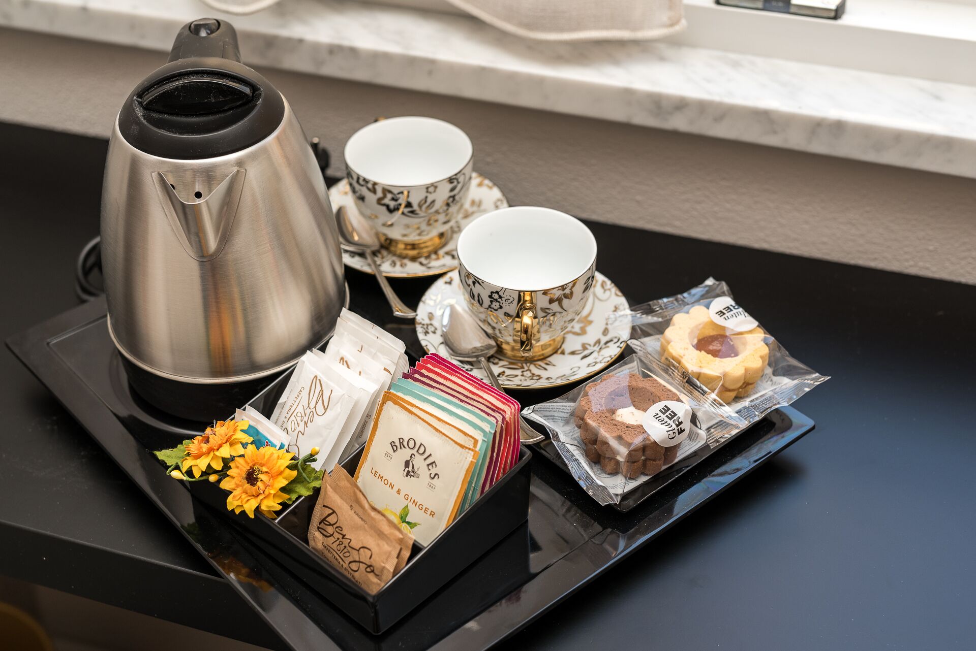 Un plateau avec une cafetière, des tasses à thé, une fleur et des en-cas emballés.