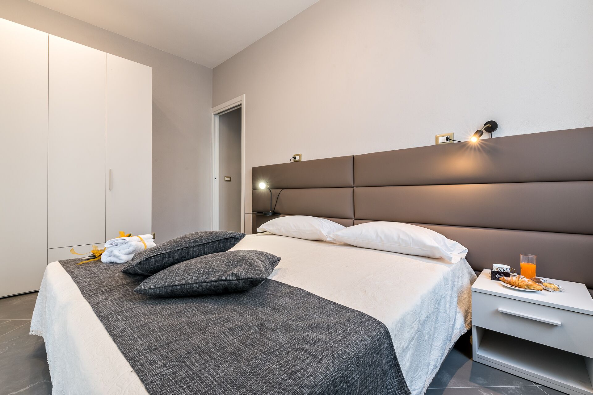 Un dormitorio moderno con una cama grande, una mesita de noche con lámpara y un armario.