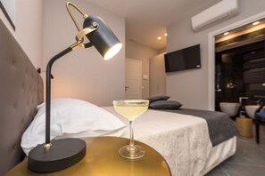 Un lit bien fait, recouvert d’une couette blanche, une lampe de chevet et un verre à martini posés sur une table de chevet dorée.