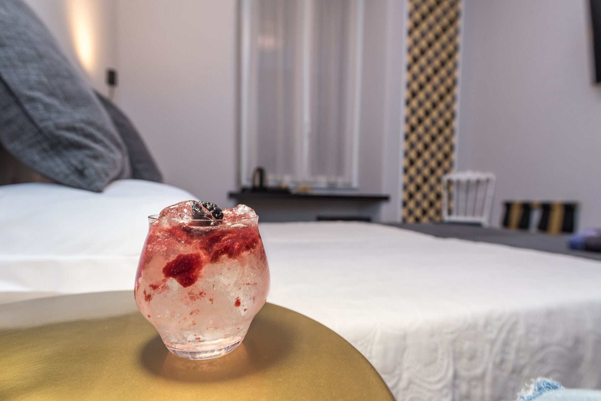 Un vaso de bebida roja con hielo sobre una cama en una habitación de hotel.