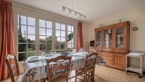 Een eethoek met een tafel voor vier personen, houten stoelen, een kast met glazen deuren en uitzicht op groen.