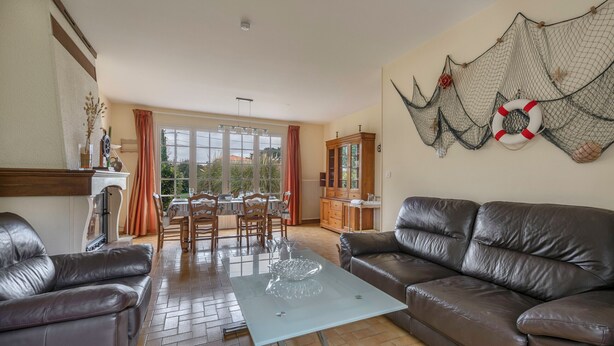 Een woonkamer met een bruine leren bank, een glazen salontafel en een eethoek met een tafel en stoelen.