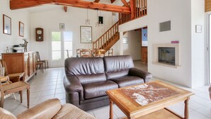 A spacious living room with a leather sofa, wooden coffee table, and a staircase with wooden beams. - Les Portes en Ré, house with garden for 7 (Les Portes-en-Ré)