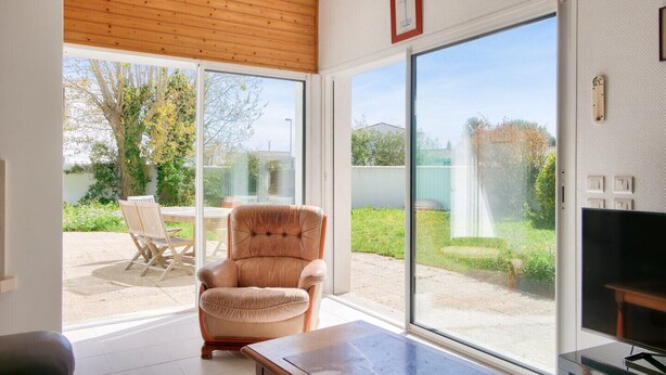 A spacious living room with a large sliding glass door leading to a patio, a comfortable armchair, a coffee table, and a television. - Les Portes en Ré, house with garden for 7 (Les Portes-en-Ré)