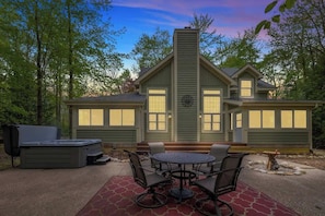Une maison à deux étages dotée d’un patio comprenant une table ronde et des chaises, un barbecue et un jacuzzi.