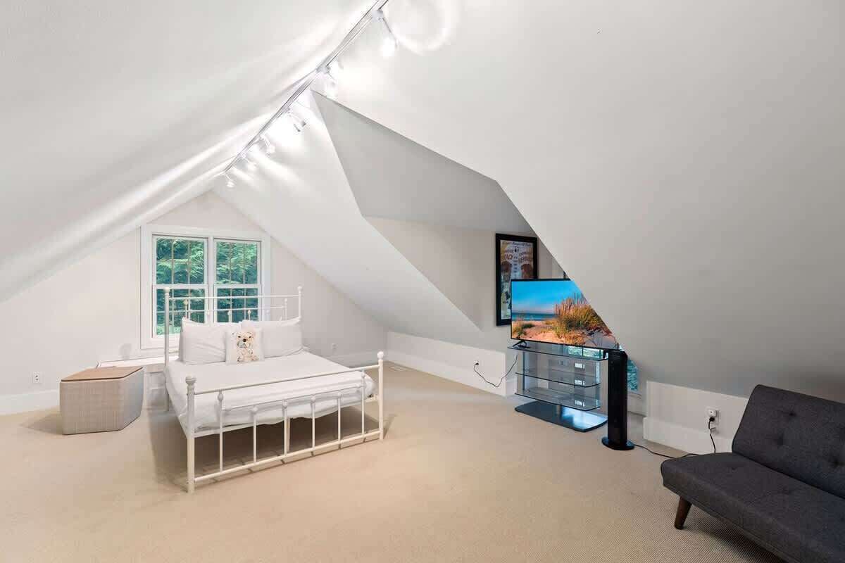 A bedroom with a sloped ceiling, a bed, a TV, and a sofa.