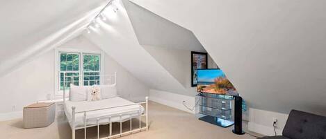 A bedroom with a sloped ceiling, a bed, a TV, and a sofa.
