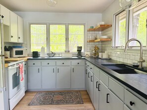 Una cocina moderna con armarios blancos, encimera negra, pileta de acero inoxidable y ventana con vista a árboles.