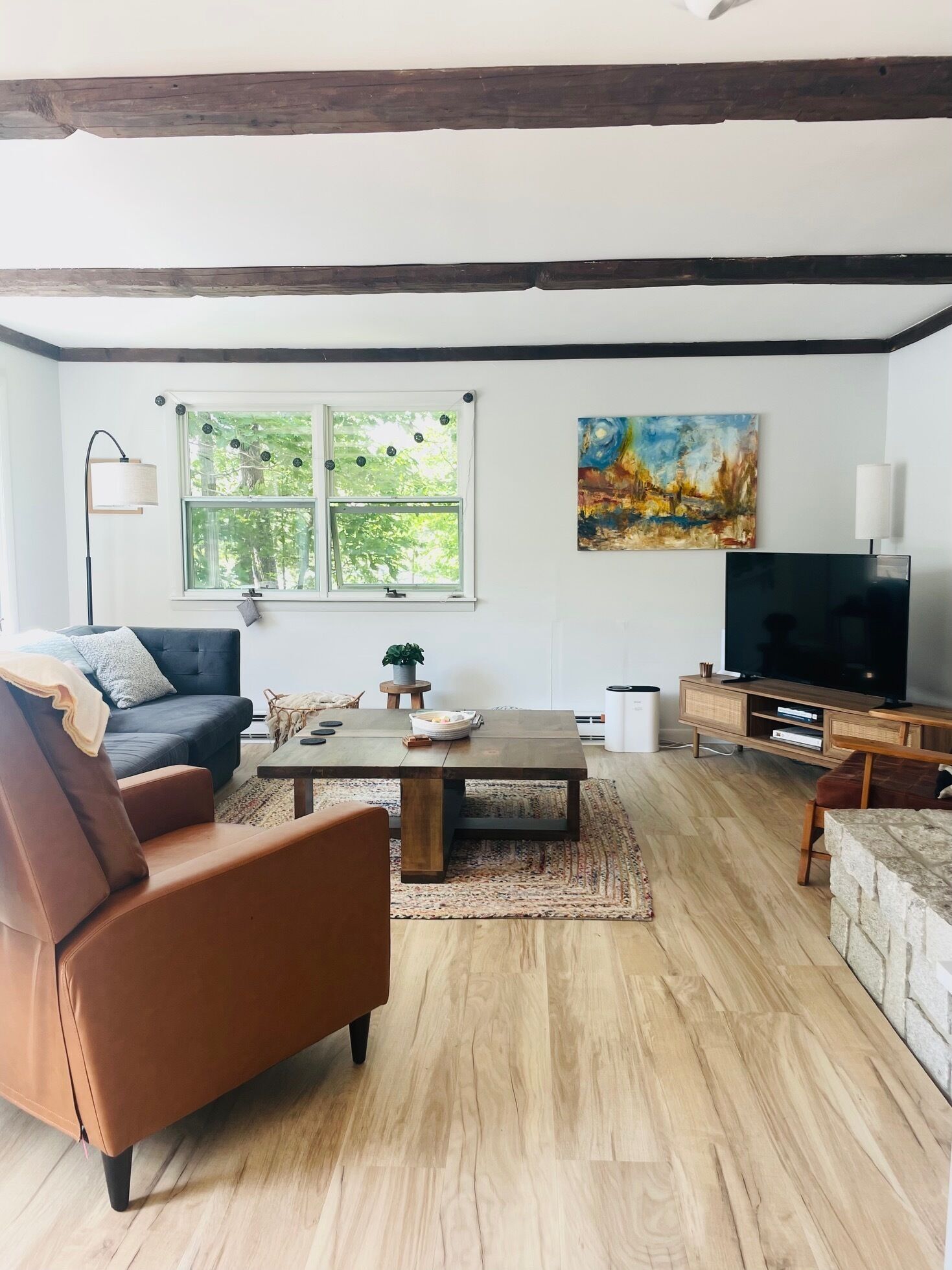 A modern living room with a dark sofa, a wooden coffee table, a TV stand, and a painting on the wall.