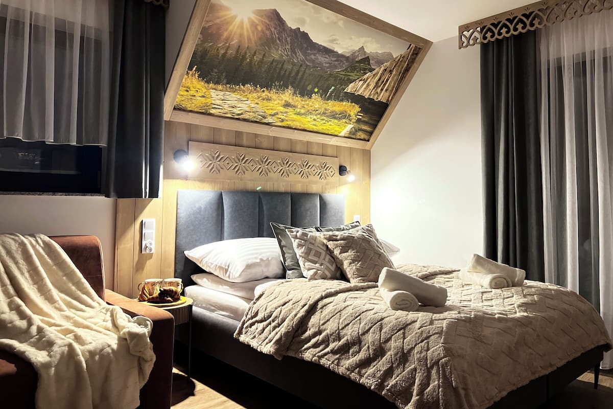 A bedroom with a bed, a nightstand, a TV, and a painting of a mountain landscape.