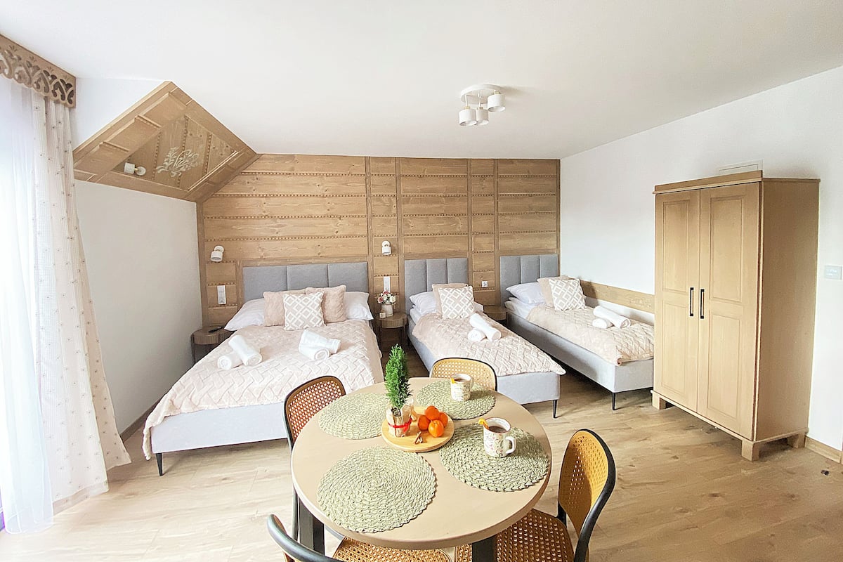 A bedroom with two beds, a dining table with placemats, and a wardrobe.