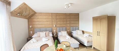 A bedroom with two beds, a dining table with placemats, and a wardrobe.