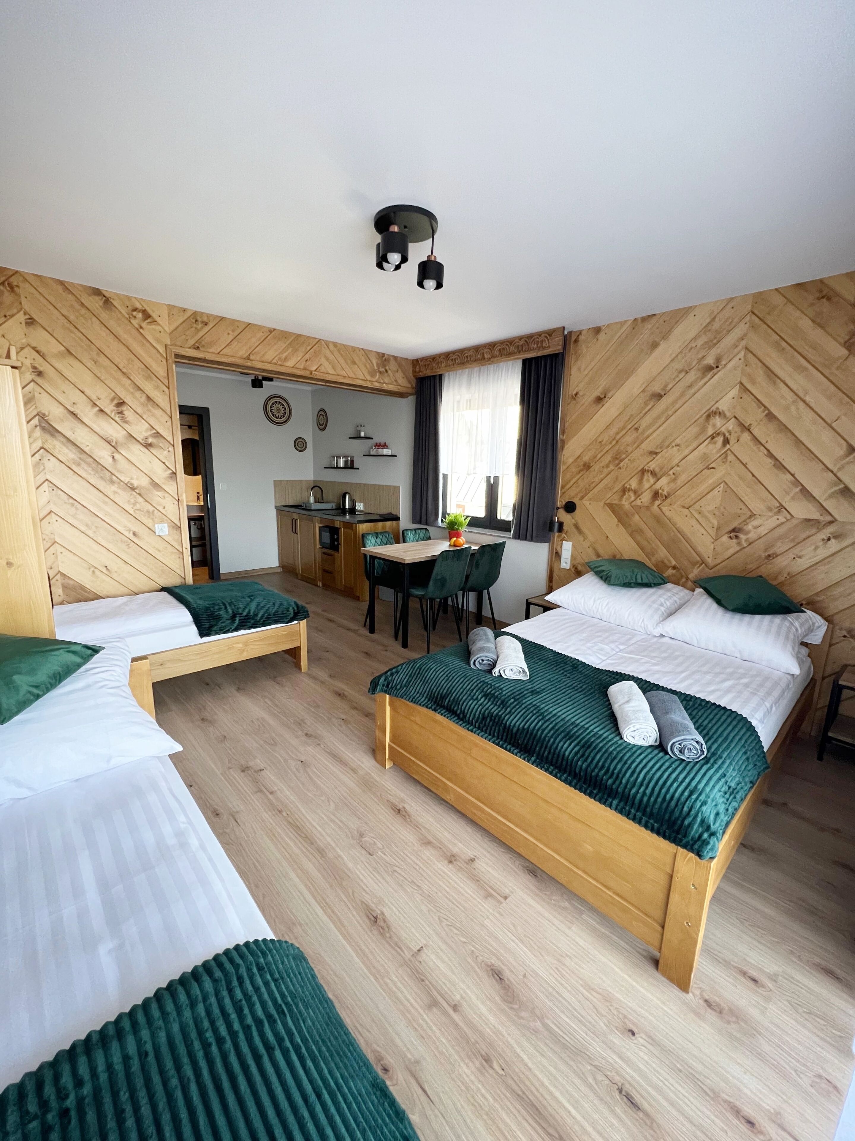 Habitación de hotel con dos camas de madera, un pequeño espacio kitchenette, una mesa de comedor y una zona de estar separada.