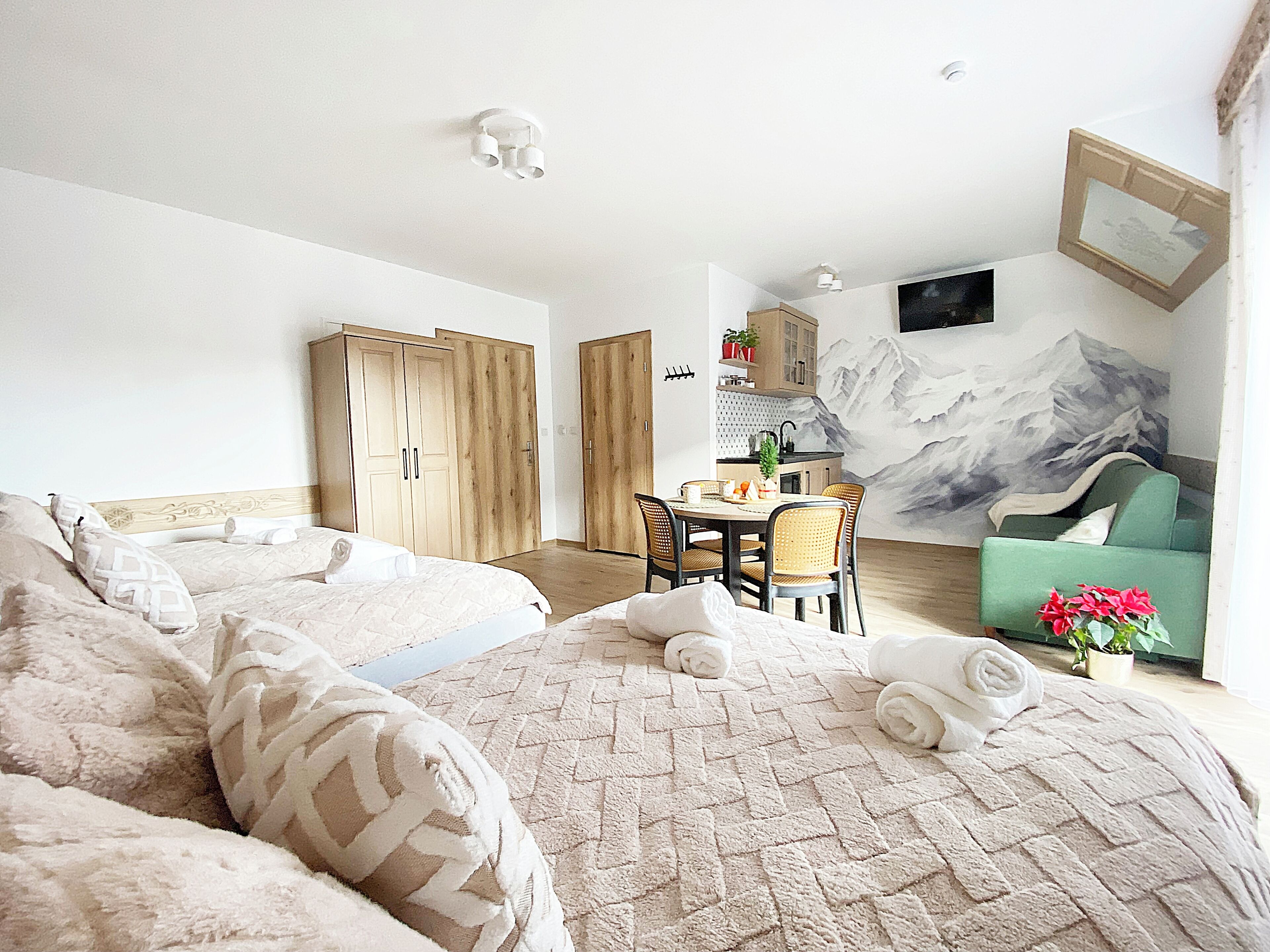 A hotel room with two beds, a dining area, a kitchen, and a living area with a mountain mural.