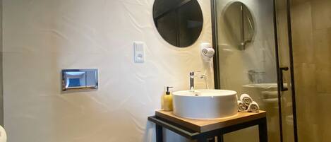 A modern bathroom with a white toilet, a round mirror, a sink with a wooden countertop, and a glass shower enclosure.