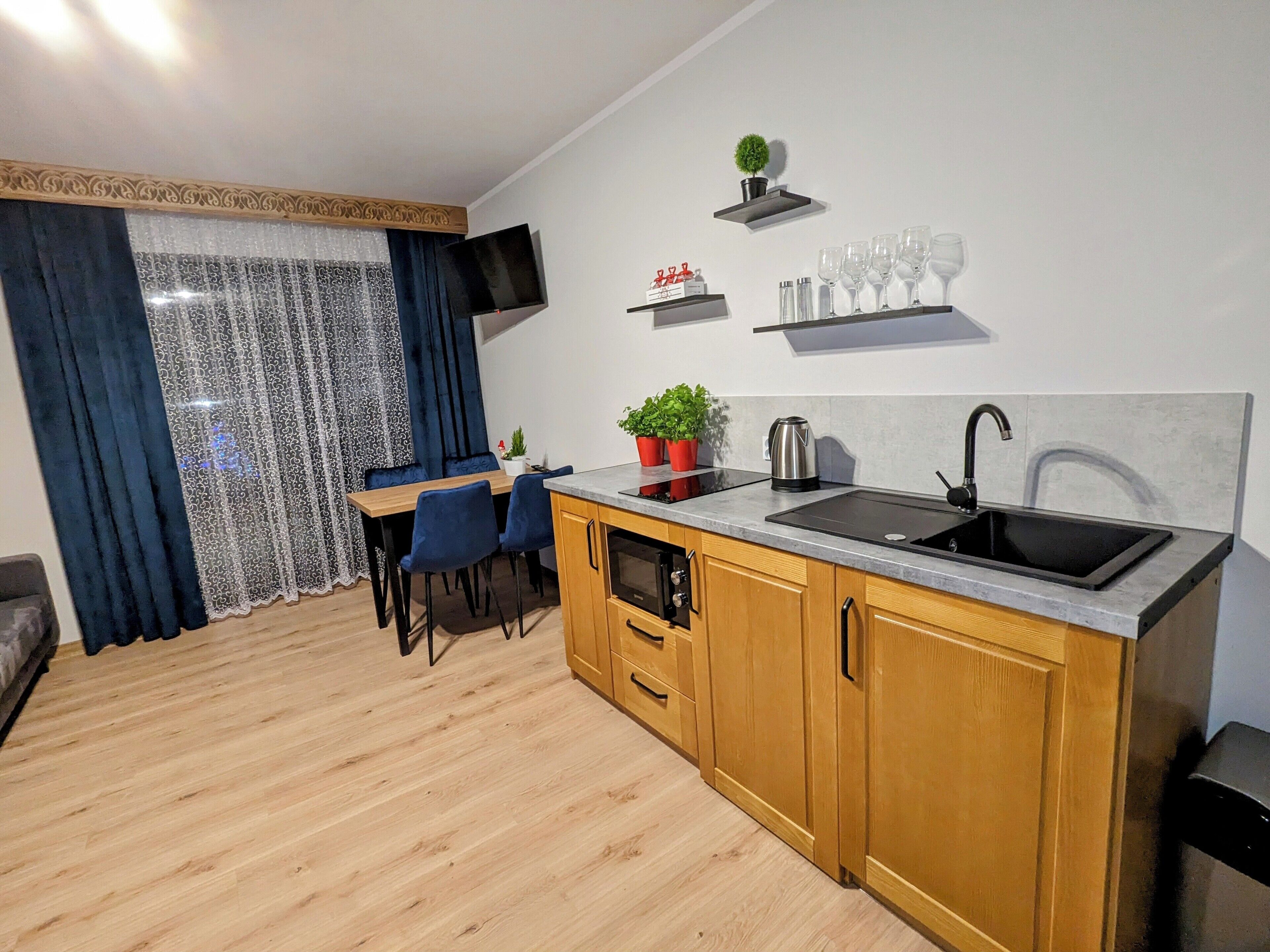 Una cocina compacta con armarios de madera, un lavamanos negro y una zona de comedor con sillas azules.