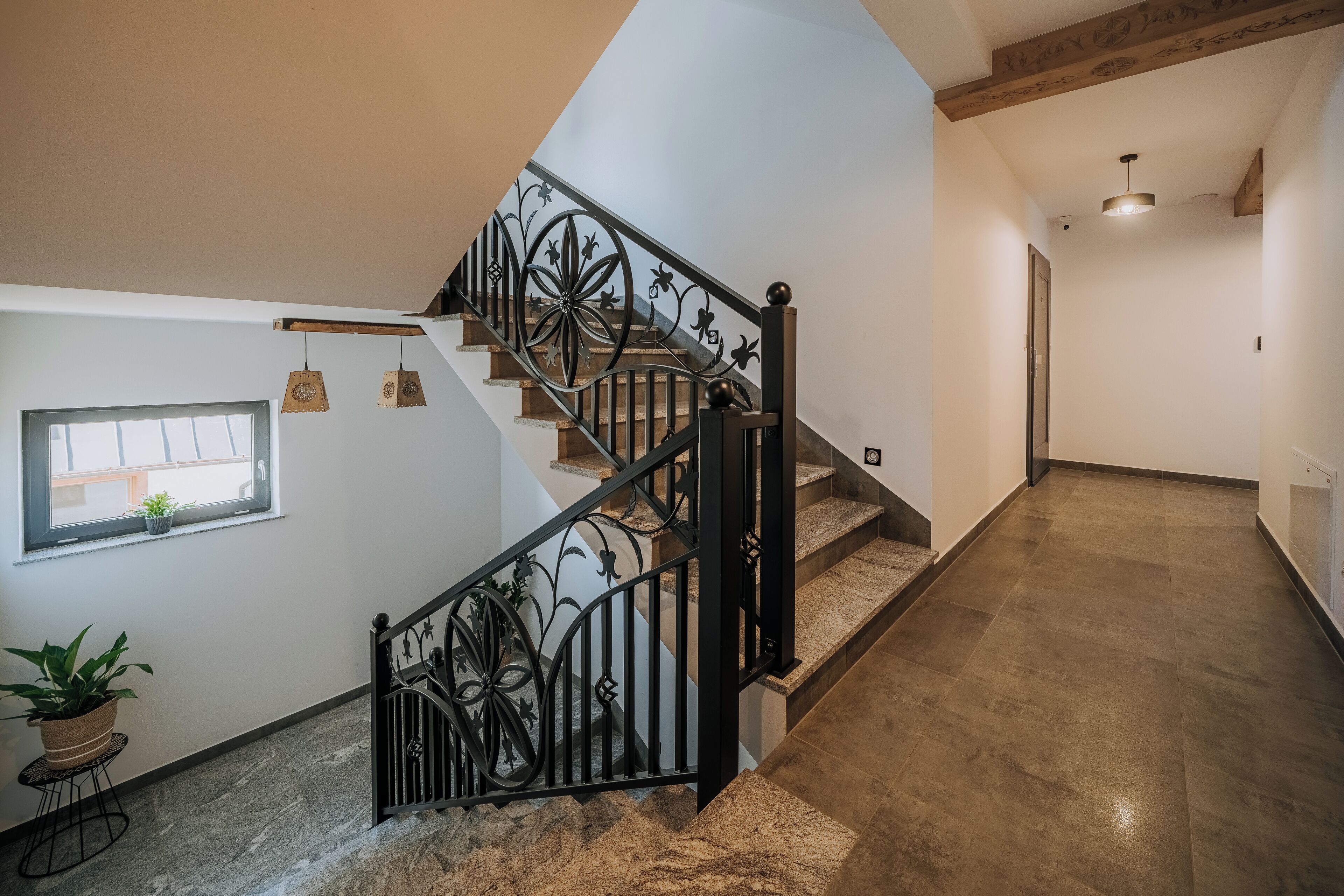 A staircase with black wrought iron railings and wooden steps, leading to a landing with a potted plant and a small window.
