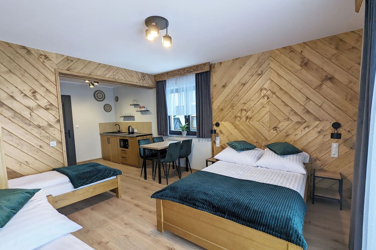A room with two beds, a dining table, and a kitchenette.