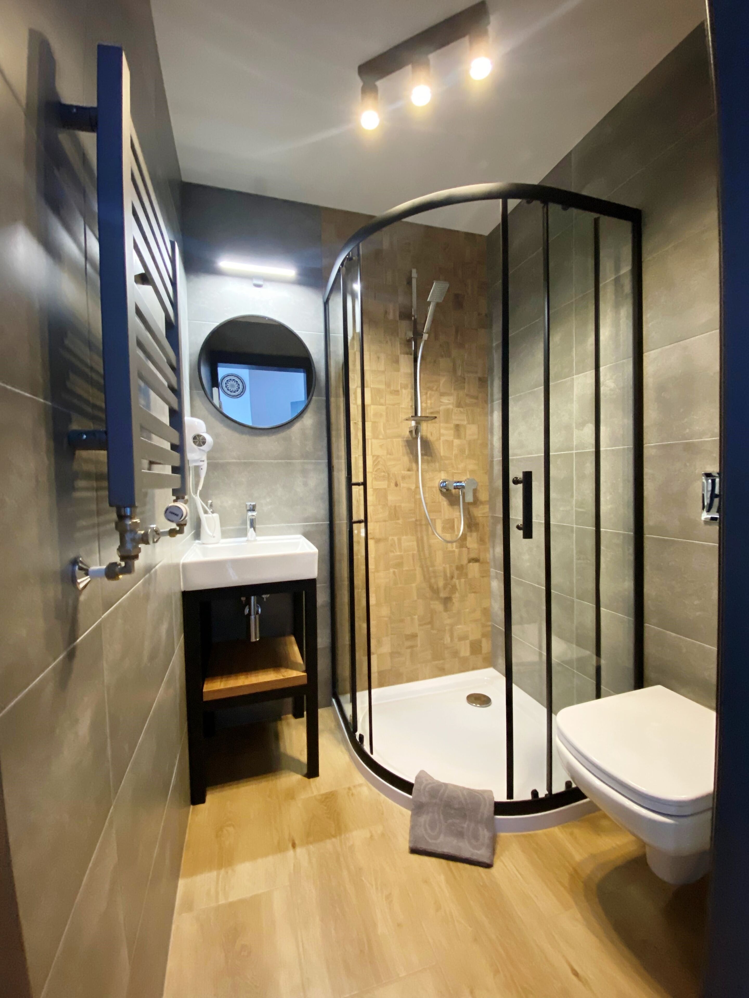 A modern bathroom with a glass-enclosed shower, a round mirror, and a white sink.