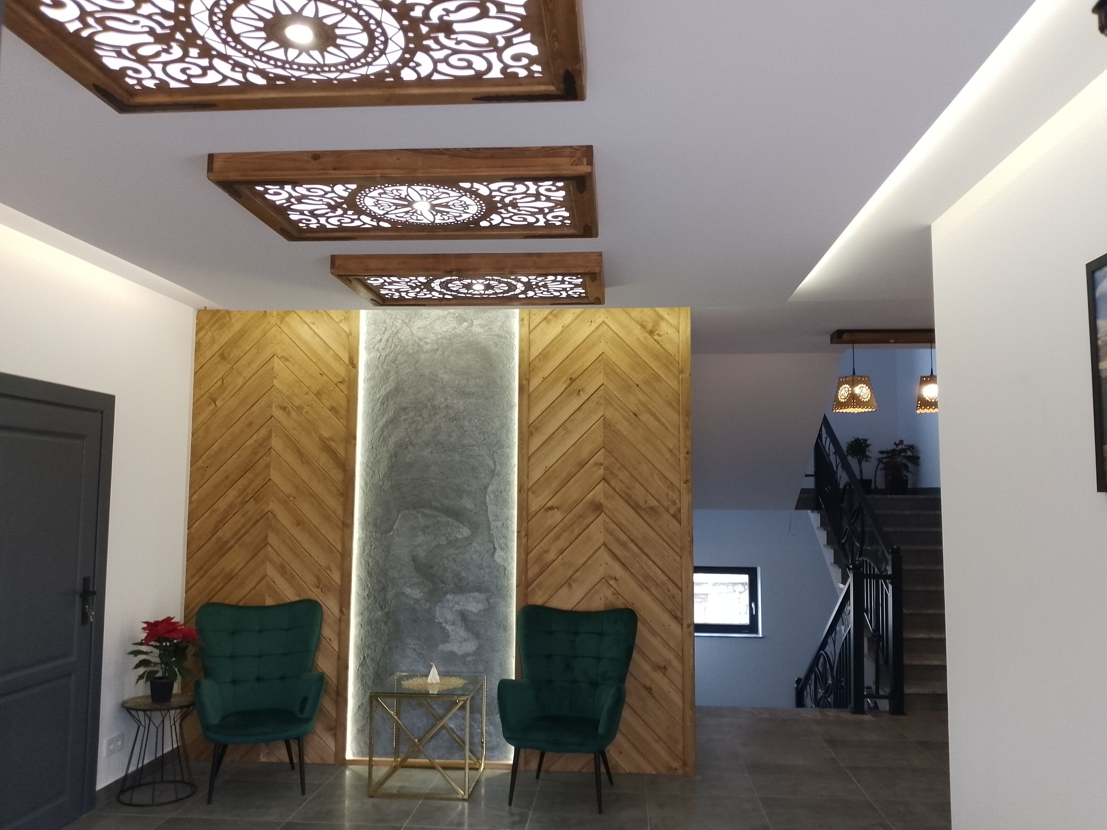 A modern interior with a wooden herringbone wall, a central vertical light feature, and two green chairs.