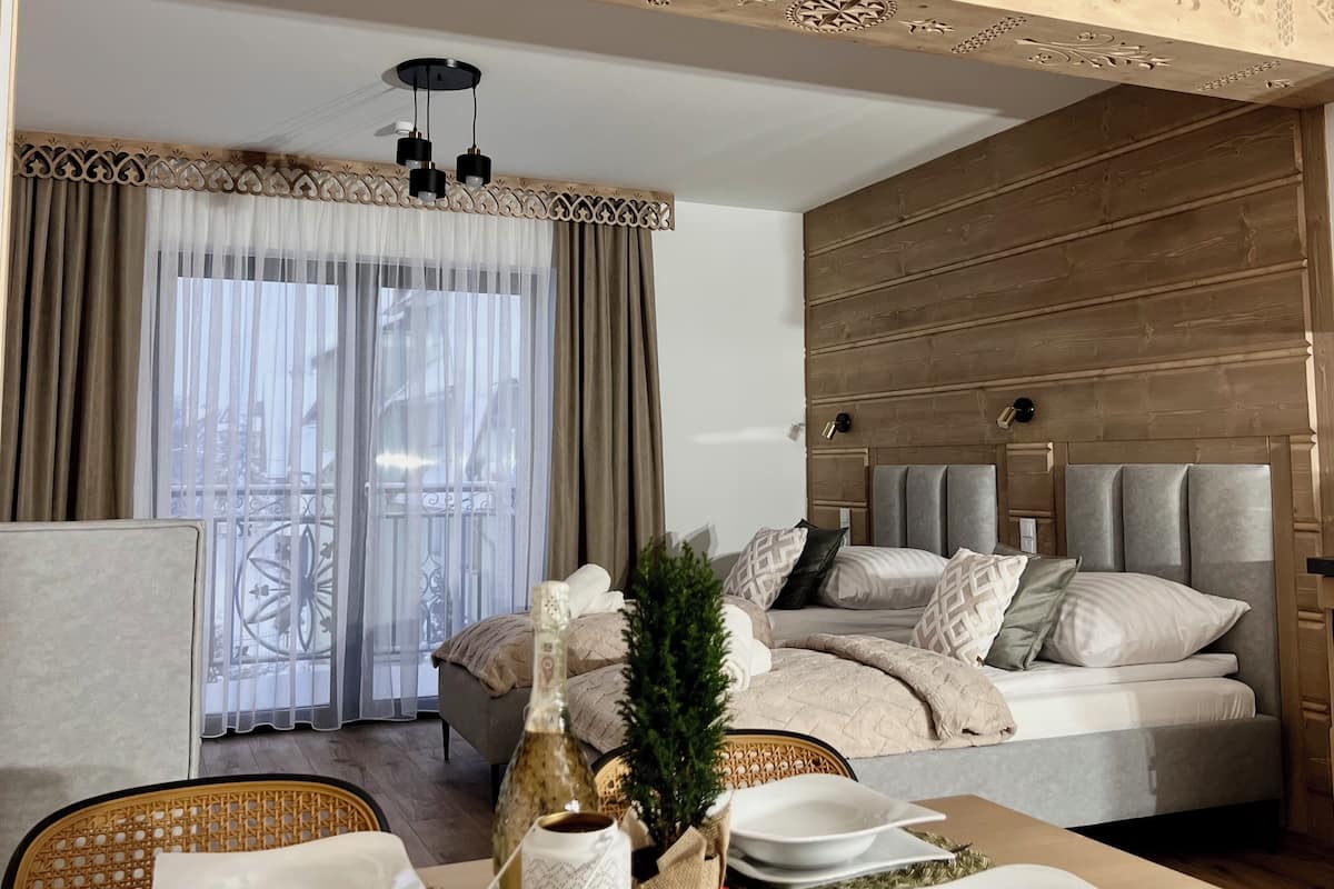 A modern hotel room with a large bed, a dining table set with plates and a bottle, and a balcony with a view.