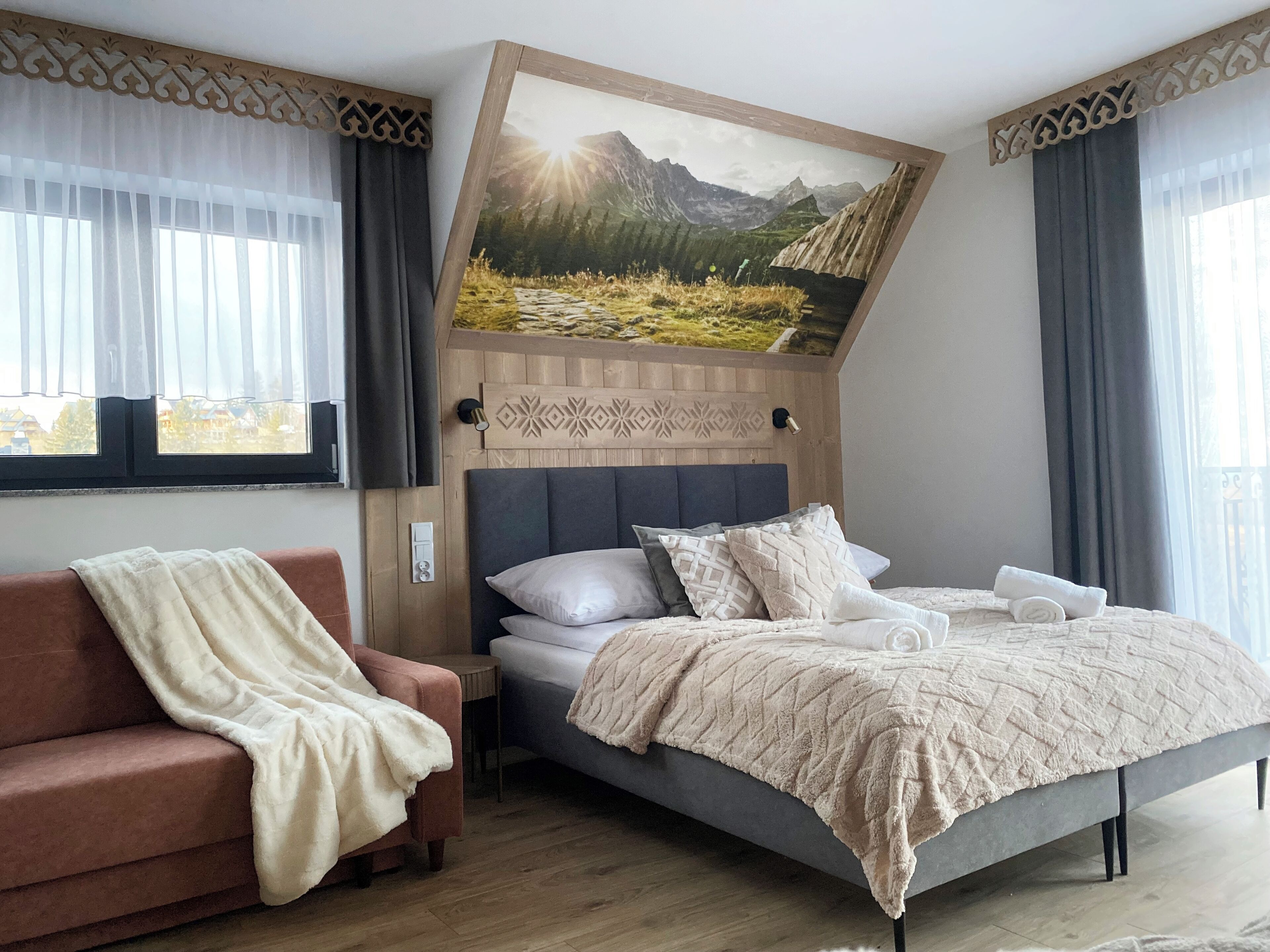 Une chambre moderne avec un lit, un canapé et un grand tableau représentant un paysage montagneux, accroché au mur.