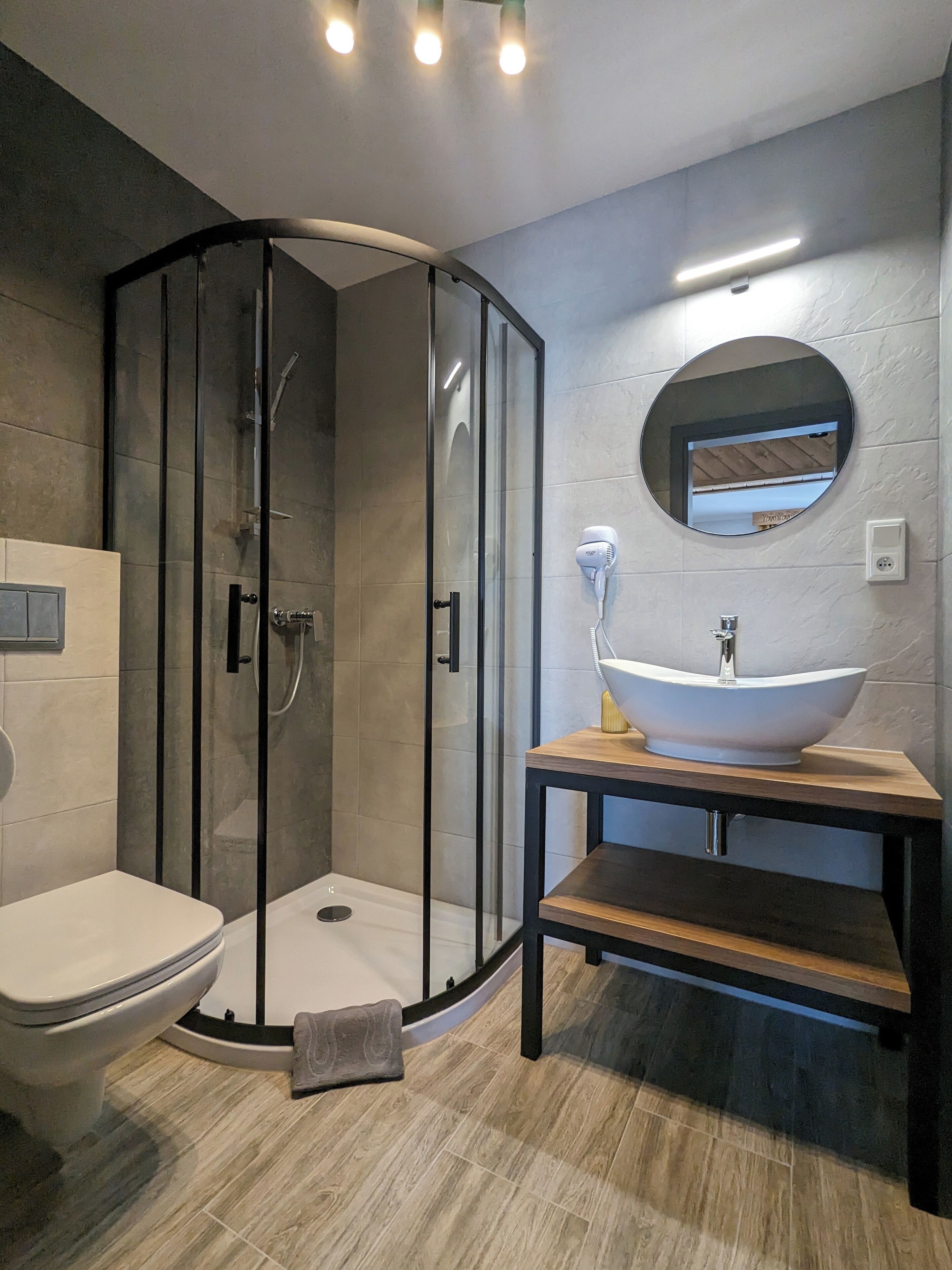 A modern bathroom with a glass-enclosed shower, a round mirror, a vessel sink, and a toilet.
