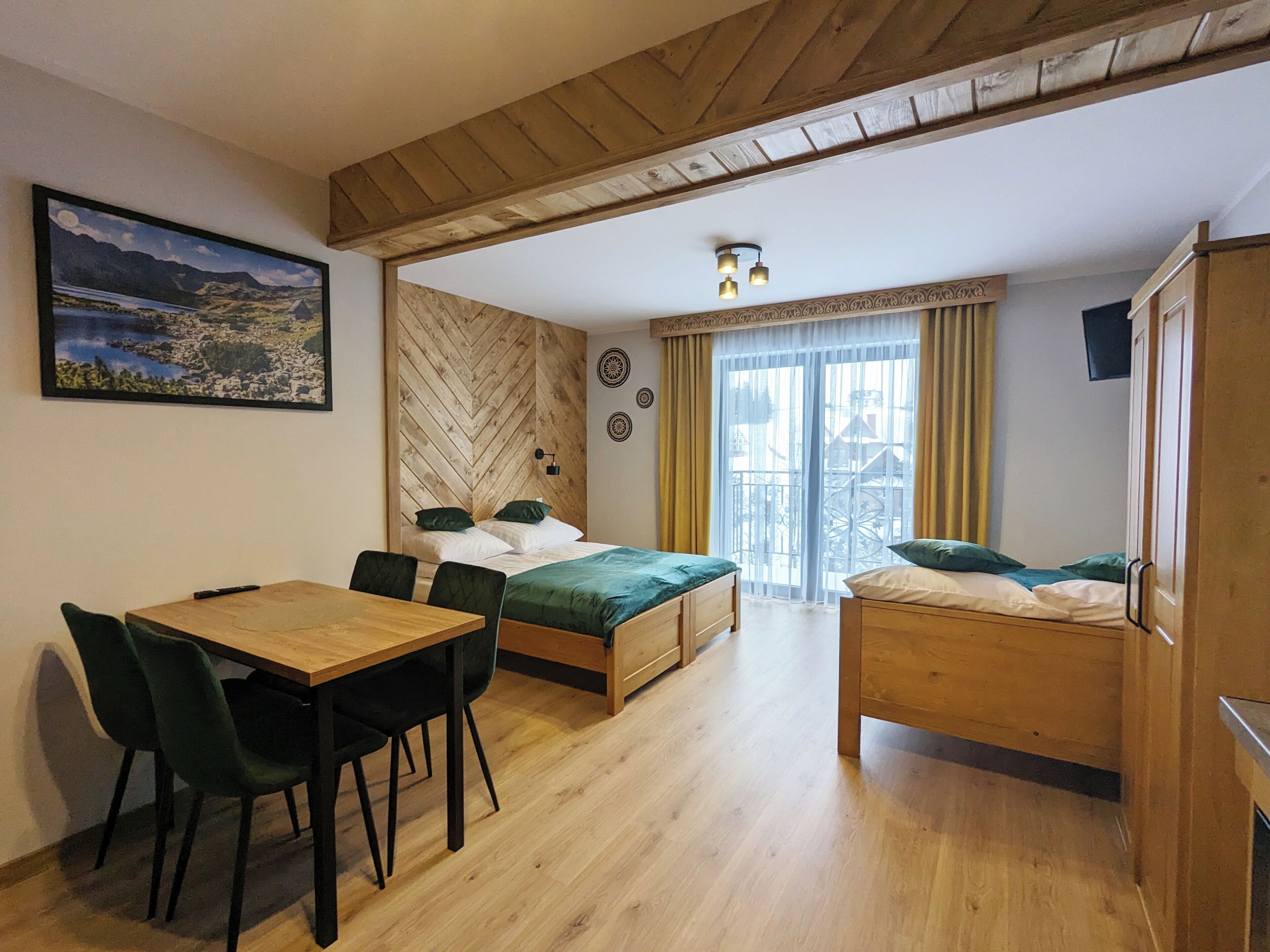 Une pièce avec deux lits en bois, une table à manger en bois avec des chaises, un tableau accroché au mur et une vue sur l’extérieur par une fenêtre.