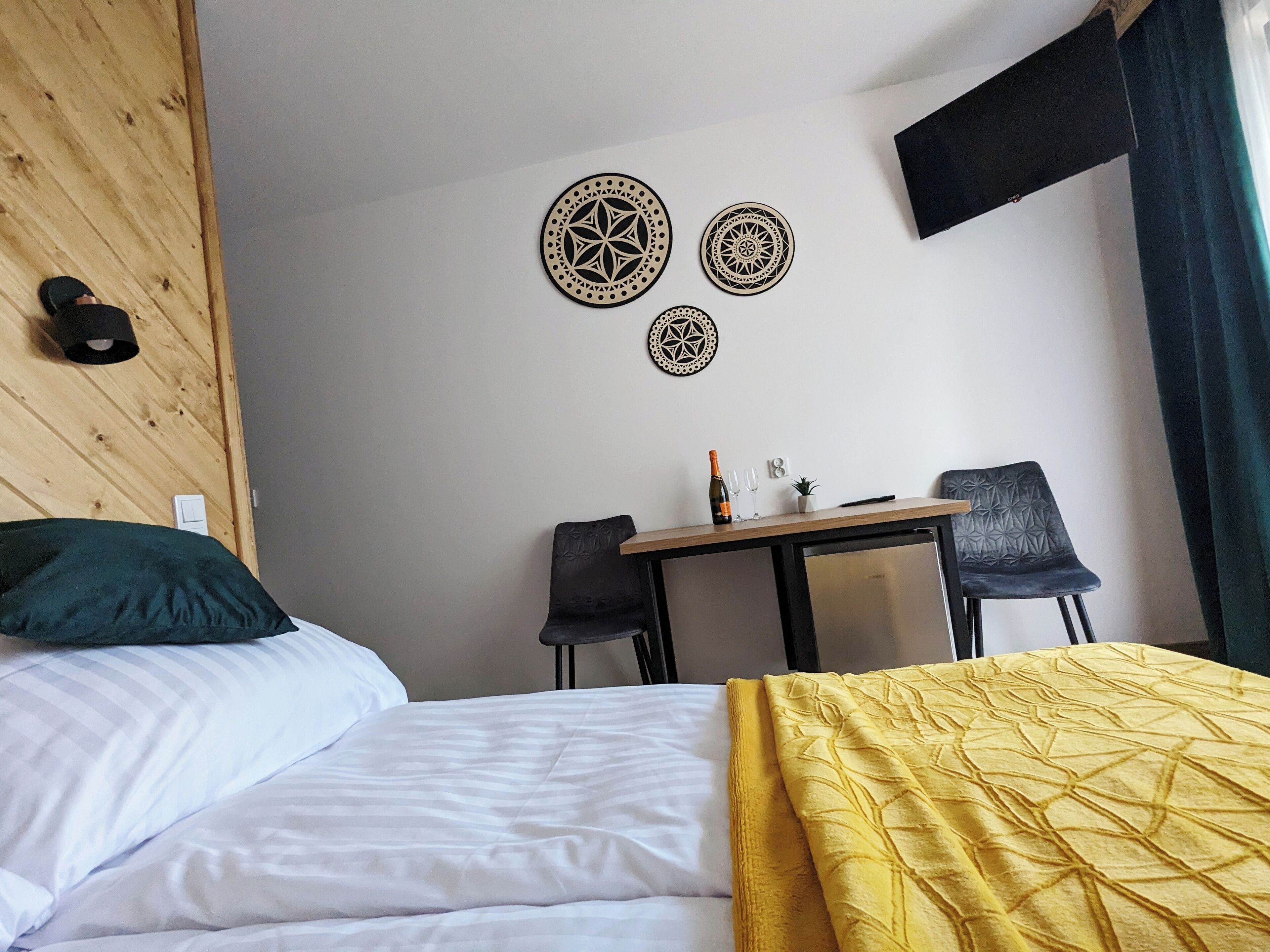 A hotel room with a bed, two chairs, a small table with a bottle and glasses, and decorative wall art.