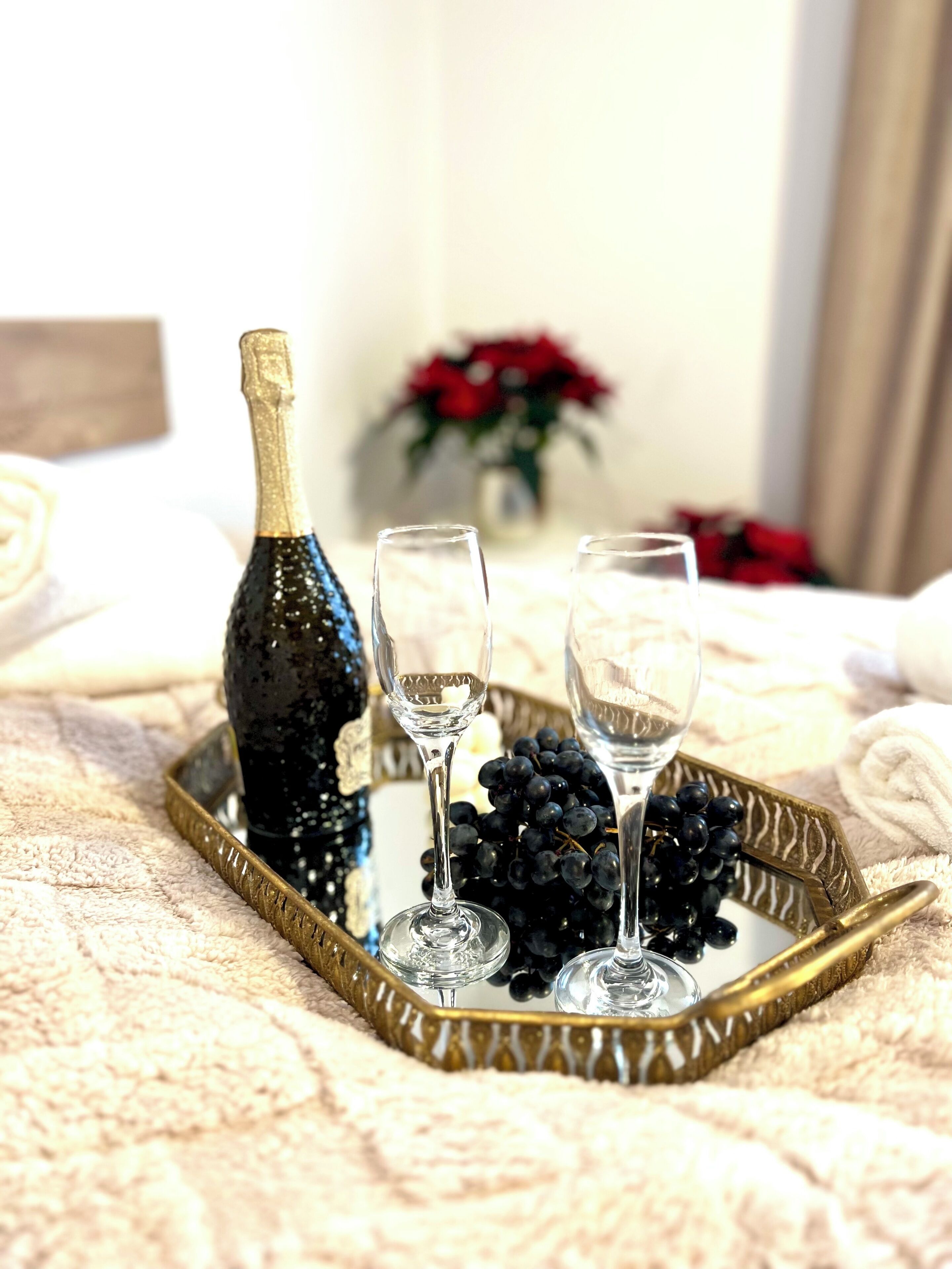 A bottle of champagne, two glasses, and a bunch of grapes on a tray.