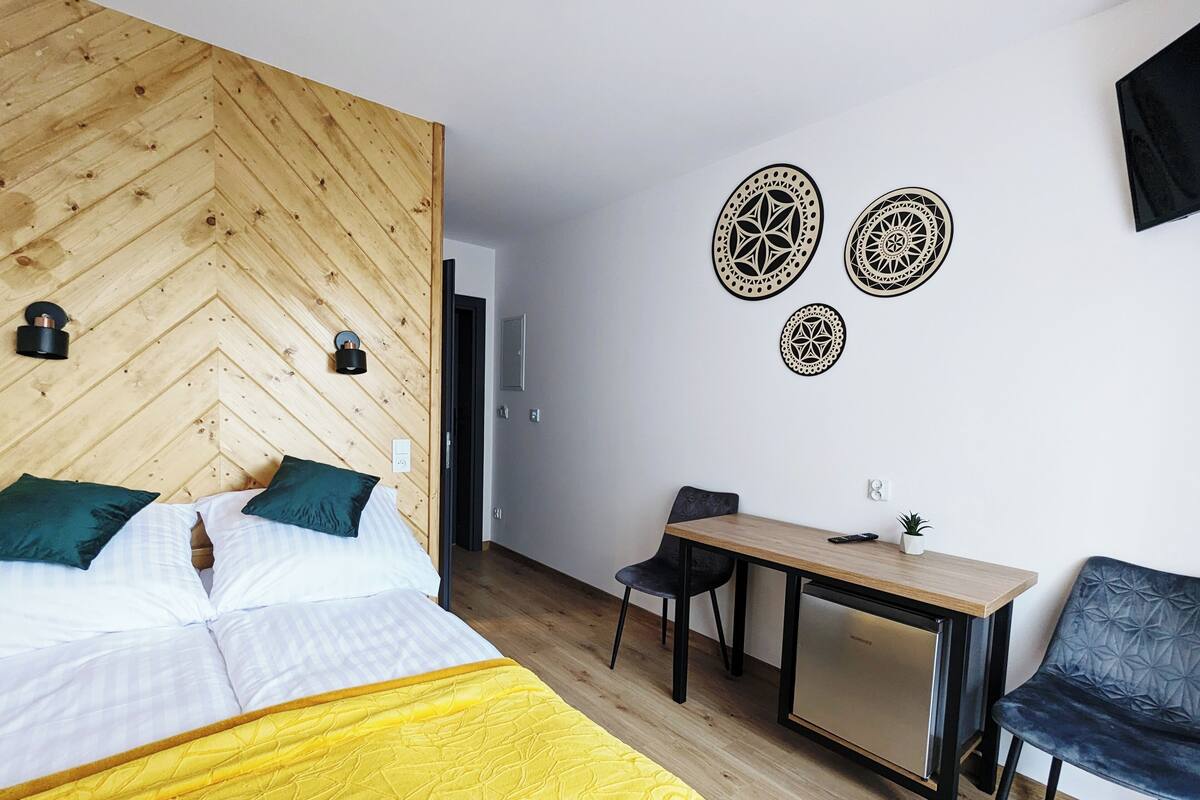 A hotel room with a bed, a desk, and a chair. There are decorative wall art pieces and a small plant on the desk.