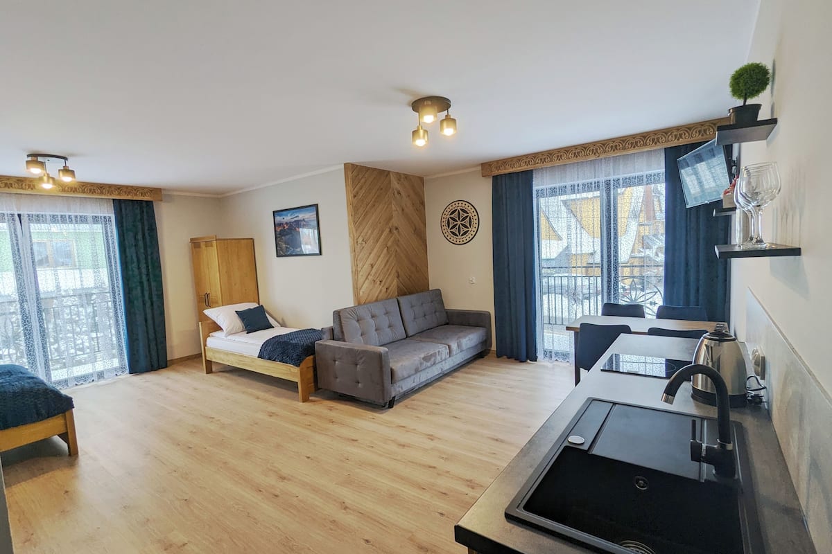 A modern, well-lit room with a bed, sofa, and kitchenette.