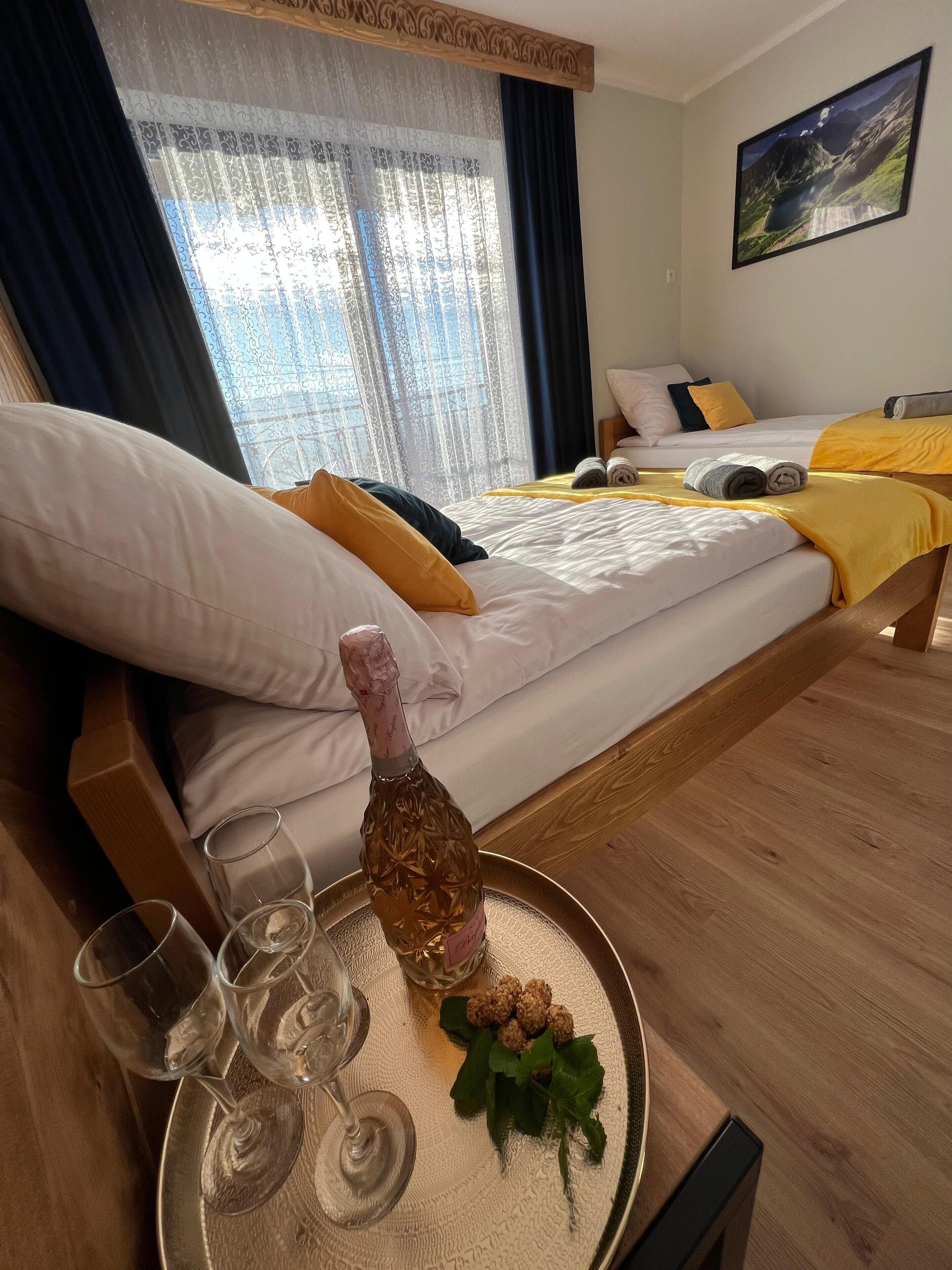 Una habitación de hotel con una cama, una mesa de comedor con una botella y vasos, y una ventana con cortinas.