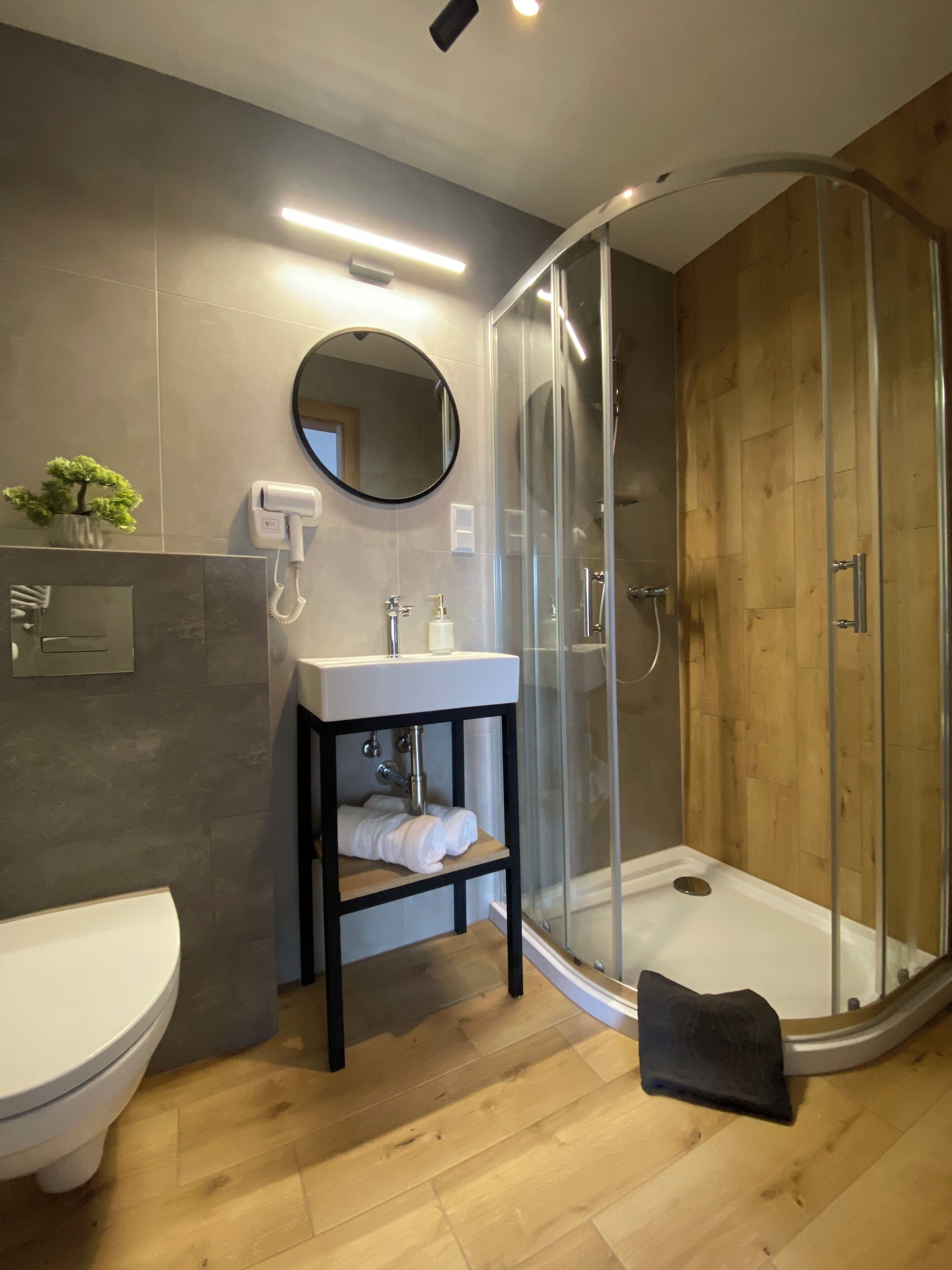 Et moderne badeværelse med en glasvæg omkring brusebadet, en hvid vask og et toilet.