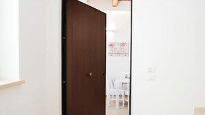 A hallway with a wooden door leading to a room with a white table and chairs. - Appartamento Viale Patrono D'italia (Santa Maria degli Angeli)