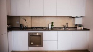 A modern kitchen with white cabinets, a built-in oven, a sink, and a stove. - Appartamento Viale Patrono D'italia (Santa Maria degli Angeli)