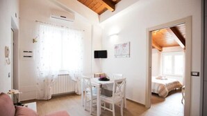 A bright, well-lit room with a dining table and chairs, a bed, and a small kitchenette. - Appartamento Viale Patrono D'italia (Santa Maria degli Angeli)