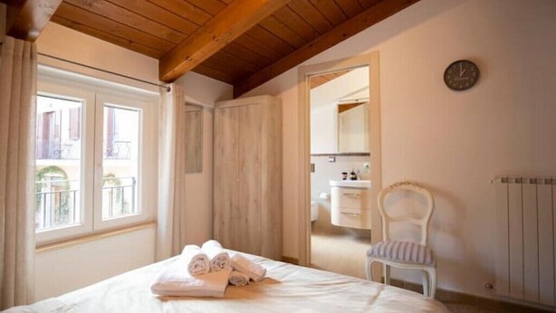 A bedroom with a wooden ceiling, a bed with rolled towels, a chair, and a bathroom visible through an open door. - Appartamento Viale Patrono D'italia (Santa Maria degli Angeli)