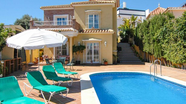 Un espace piscine avec des chaises longues vertes, un parasol blanc et un escalier menant à un balcon.