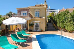 A pool area with green lounge chairs, a white umbrella, and a staircase leading to a balcony. - Villa Mercedes Nerja (Nerja)
