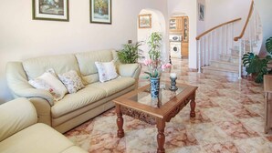 Un salon avec un canapé beige, une table basse en verre et un sol en marbre.