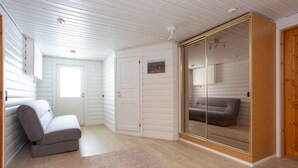 Een kamer met een grijze bank, een witte deur en een schuifdeur van glas die naar een andere kamer leidt.