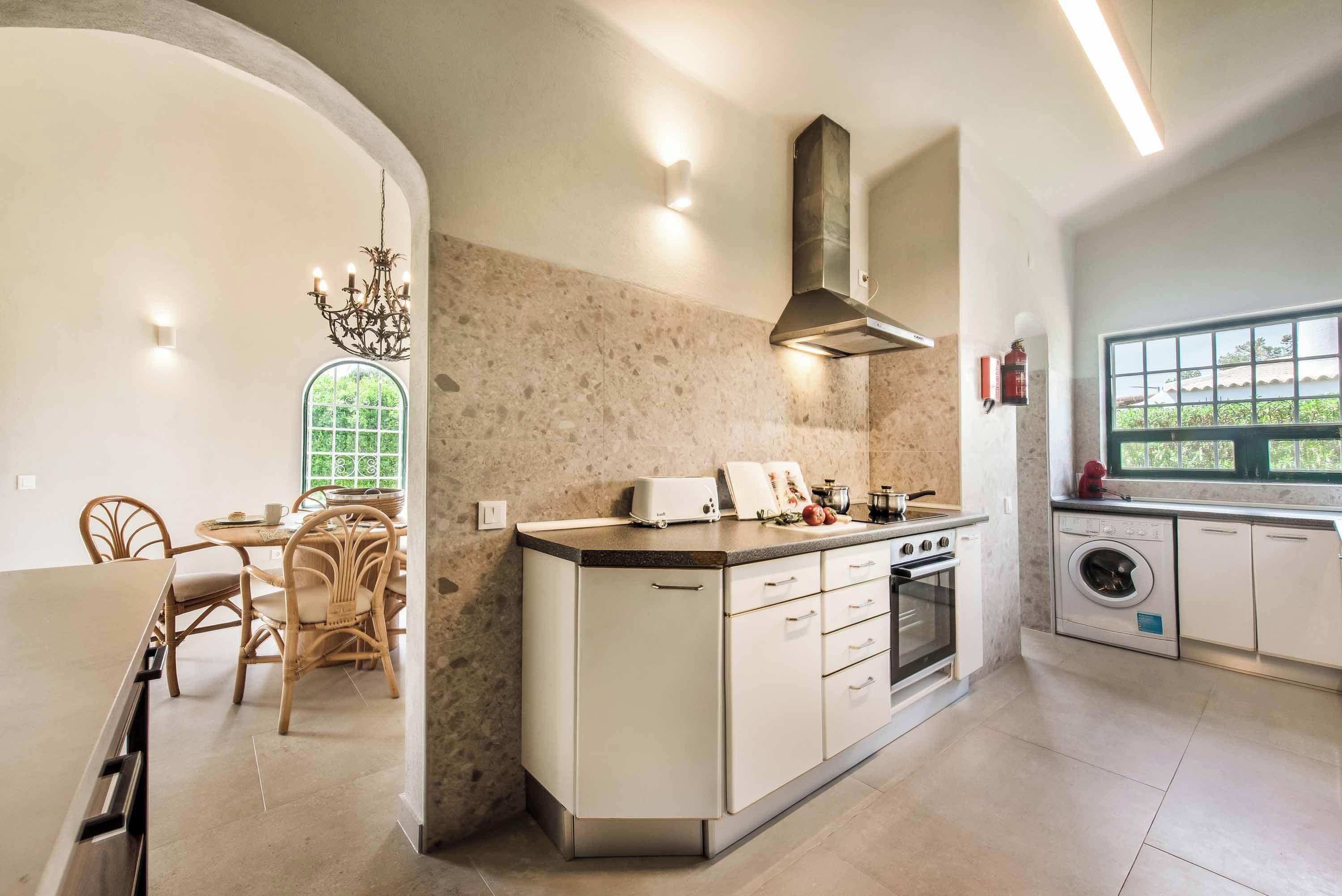 A kitchen with a central island, a dining area with chairs, a window, and a built-in washing machine.