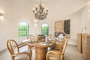 Een eetruimte met een ronde tafel, stoelen, een kroonluchter en kunstwerken aan de muur.