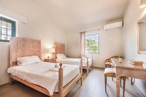 Une chambre d’hôtel avec deux lits en bois, un bureau, une chaise, une fenêtre avec des rideaux et un appareil de climatisation.