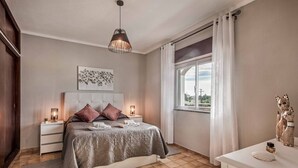 Un dormitorio con cama, mesitas de noche, ventana y lámpara colgante.