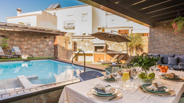 Un espace repas aménagé au bord de la piscine, avec une table pour deux, un barbecue et des chaises longues.