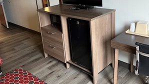 Une chambre d’hôtel avec un bureau en bois, une télévision, un petit réfrigérateur, une lampe et un tapis rouge et gris à motifs.